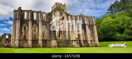 Panorama of Fountains Abbey Cistercian monastery church with tower and Chapel of Altars and group of school children North Yorkshire England Stock Photo