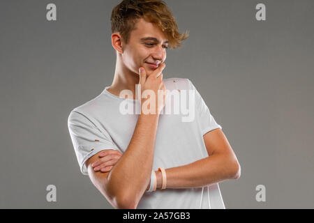 handsome emotional teenager boy posing in studio against gray, guy in a gray t-shirt with a dreamy look Stock Photo