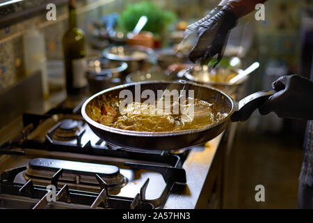 Food concept. The chef mixes spaghetti quickly in a pan the tomatoes and oysters, hands move and blur. The process of cooking spaghetti with seafood. Stock Photo