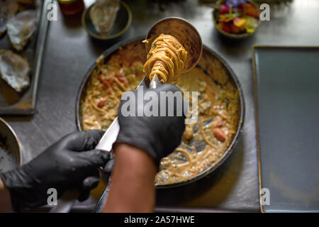 Food concept. The chef mixes spaghetti in a pan the tomatoes and oysters, dish in a restaurant. The process of cooking spaghetti with seafood. Stock Photo