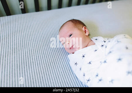 A newborn baby laying in his crib while swaddled Stock Photo