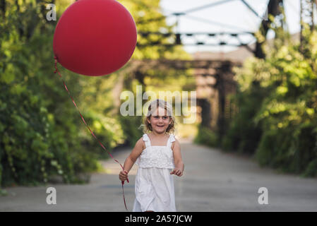 Young girl in sundress with red balloon running across steel bridge Stock Photo