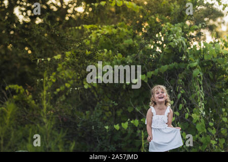 Laughing young girl in white dress with backdrop of thick foliage Stock Photo