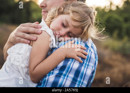 Sleeping child snuggles on her dad's shoulder in a sunny meadow