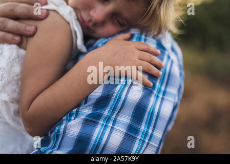 Sleeping child snuggles on her dad's shoulder in a sunny meadow