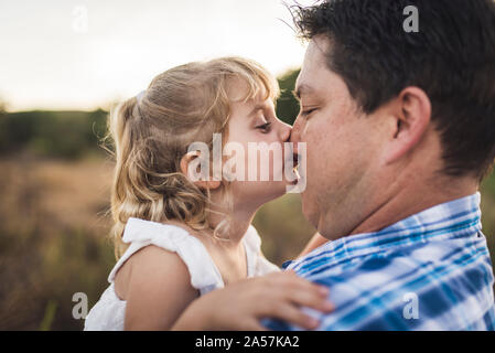 Silly young girl kissing her dad's nose outdoors in meadow Stock Photo
