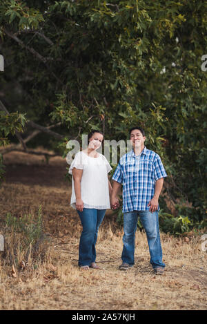 Smiling husband and wife standing under tree holding hands Stock Photo