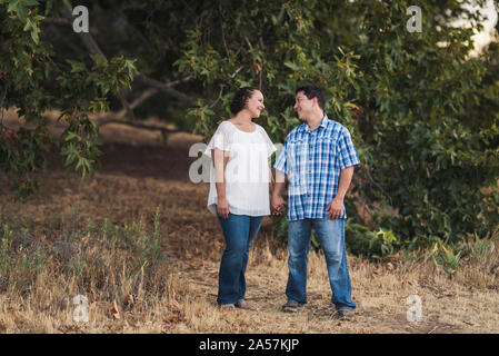 Couple gazing into each other's eyes holding hands near tree branches Stock Photo