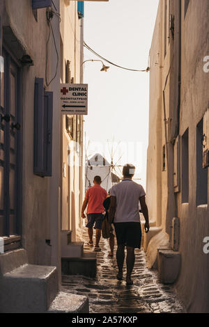 Mykonos, Greece - September 23, 2019: People walking towards windmills during sunset on a narrow street in Hora (Mykonos Town), capital of the island Stock Photo