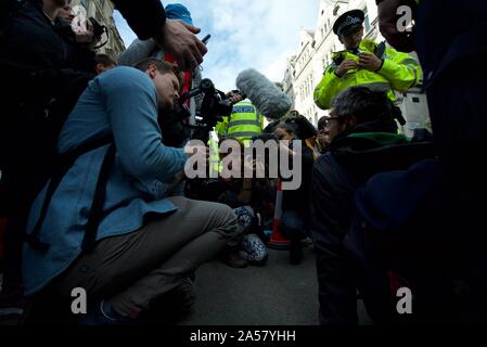 A climate protest group member (Extinction Rebellion) getting interviewed by the media at the protests in Trafalgar Square in London, police surround. Stock Photo