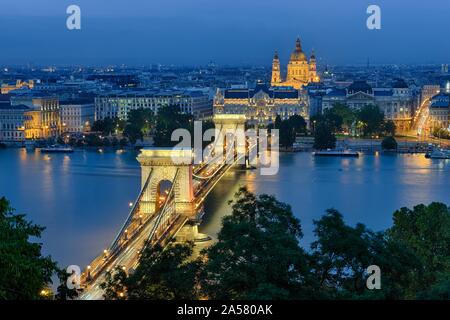 Chain bridge with Gresham Palace and St. Stephen's Basilica, illuminated, dusk, Budapest, Hungary Stock Photo