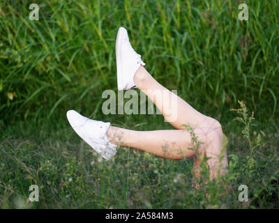 girl wearing white trainers lying in grass with legs up in the air Stock Photo