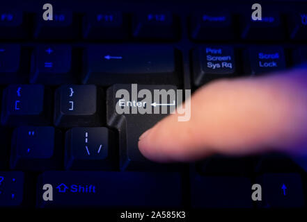Finger hacker or spy in the dark, presses the enter button on the keyboard. Stock Photo