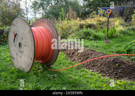 Wooden spool with fiber optic cable for fast internet ready to be laid in narrow trenches in the ground on a meadow, infrastructure expansion in the c Stock Photo