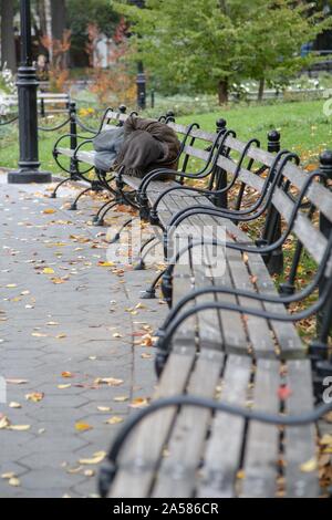 Vertical shot of a homeless person sleeping on a bench in Central park, New York City Stock Photo