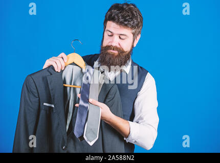 Shop assistant or personal stylist service. Stylist advice. Matching necktie with outfit. Man bearded hipster hold neckties and formal suit. Guy choosing necktie. Perfect necktie. Shopping concept. Stock Photo