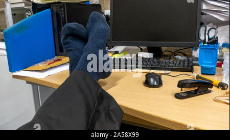 Engineer with his shoes off and his feet up on his desk at his work station Stock Photo