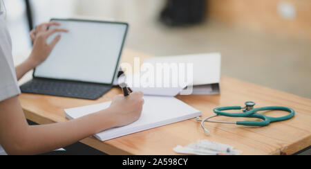 Close-up view of young female doctor examining the patient chart while using mock up tablet Stock Photo