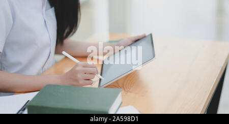 Cropped shot of young female doctor examining the patient chart while using tablet Stock Photo