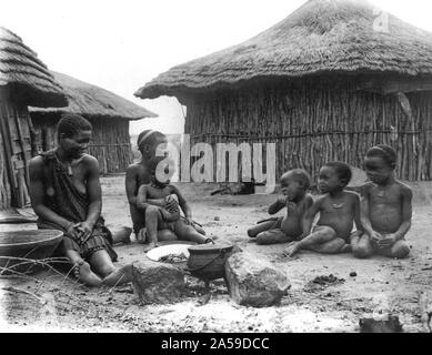 Native woman and five children in front of huts near Bulawayo, Rhodesia, Africa 1890-1925 Stock Photo