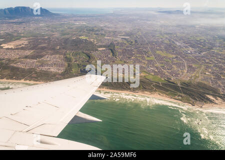 aerial view over Cape Peninsula with Table Mountain in the distance from an airplane with a wing in view and the coastline with ocean Stock Photo