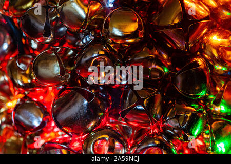 A Macro close-up image of various sized gold and chrome Jingle Bells in a glass jar with a multi-colored strand of holiday lights.  The lights illumin Stock Photo