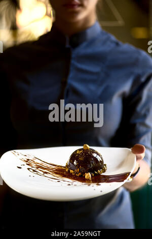 French mini mousse pastry dessert in chocolate icing on a plate. Dessert in the hands of a waitress. close up Stock Photo