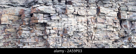 Rock cliff face background. Dangerous vertical wall with protruding crumbling layered stone blocks in quarry for the extraction of wild stone Stock Photo