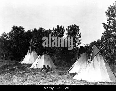 Edward S. Curtis Native American Indians - An Assiniboin camp containing four tepees with Indians seated on ground ca. 1908 Stock Photo