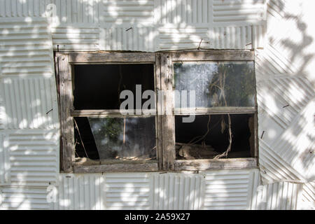 Broken glass window on white plastic tiles on the wall, outdoors. Damaged window Stock Photo