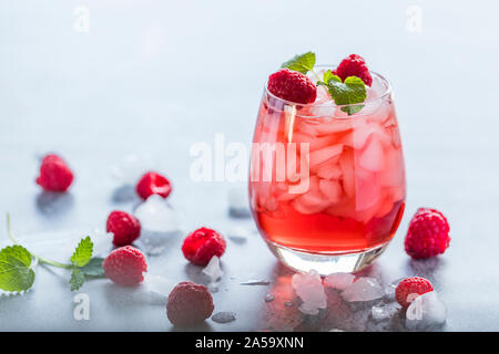 A refreshing red translucent raspberry drink with ice and fresh raspberries. The juice is garnished with a green leaf, and there are pieces of ice and Stock Photo