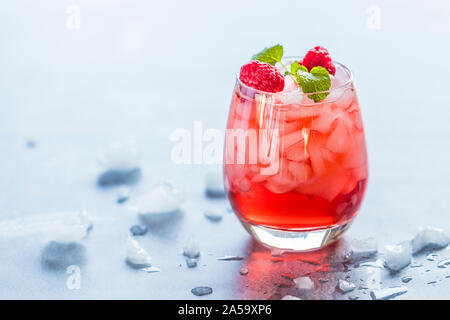 Close-up of a a refreshing red translucent drink with ice and raspberries. The juice is garnished with a green leaf, and therer are pieces of ice and Stock Photo