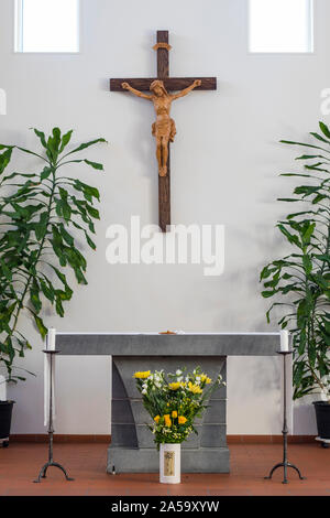 The Altar of a catholic church, in a clean design with some green plants and a bouquet of yellow flowers in front of the altar table. There is a woode Stock Photo