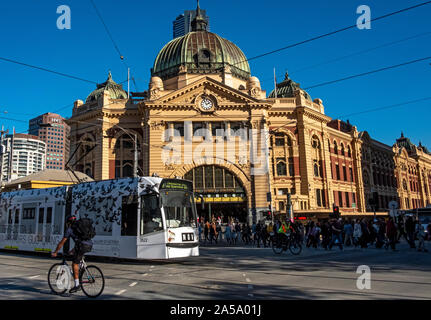 A tram and cyclist pass by Flinders Street Railway Station in Melbourne, Victoria, Australia
