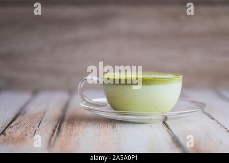 Matcha green tea latte on a wooden table. The healthy frothy tea drink is in a glass cup with a saucer, on a wooden table. The tea cup is placed sligh Stock Photo
