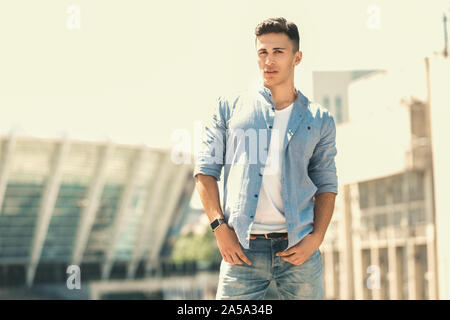 Outdoors Leisure. Stylish guy wearing watch standing on the street hands in pocket posing pensive Stock Photo