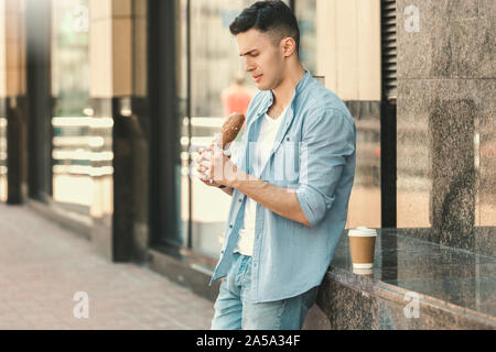 Outdoors Leisure. Stylish guy standing on the street looking at sandwich concerned Stock Photo