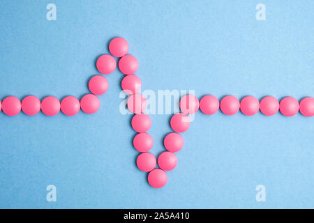 Heart cardiogram made of pink pills on blue background. Stock Photo