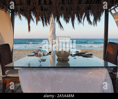 Gazebo on the beach with table set. Candle on table. Relaxing context. Nobody on the beach. Blue sea on the back. Fabulous holiday Stock Photo