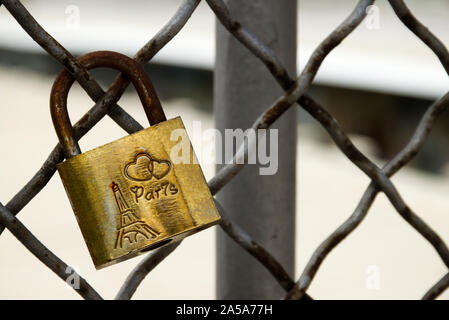 Single copper love-lock, mounted on the grey and rusty fence of a bridge in Paris, France. Usable as a background with your own text. Stock Photo