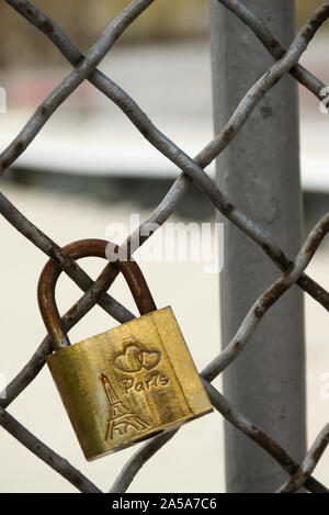 Single copper love-lock, mounted on the grey and rusty fence of a bridge in Paris, France. Usable as a background with your own text. Stock Photo