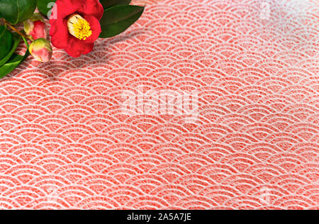 A Japanese greeting card with Tsubaki flower also called the winter rose on a traditional lace circles motif pattern on a red cloth background. Stock Photo