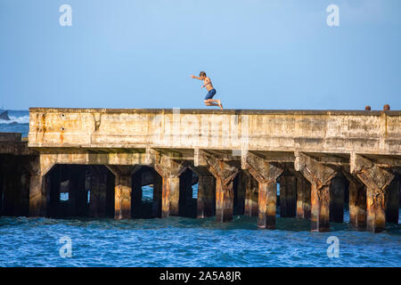 A young man, MR, jumps off the wharf in Hana Bay, Maui, Hawaii. Stock Photo