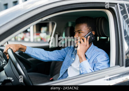 African American man using smartphone making mobile cell call during driving time in favourite luxury car. Stock Photo