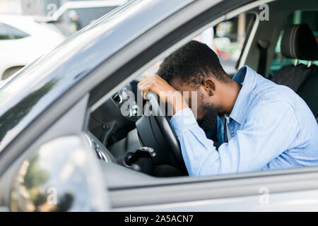 Overworked personal driver falling asleep on steering wheel of car, tired man Stock Photo