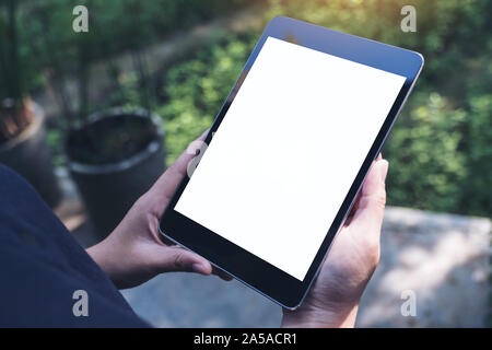 Mockup image of woman's hands holding black tablet pc with blank white screen and green nature background Stock Photo