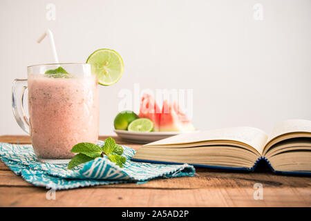 A flat lay (square ration) breakfast tabletop photo with watermelon smoothie phone, book and sliced fruit on plate -food and dieting concept image. Stock Photo