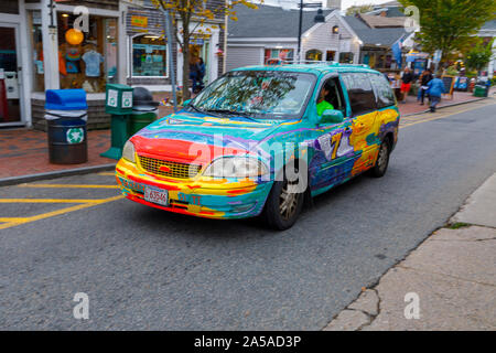 Brightly rainbow coloured spray painted car being driven through the main street of Provincetown (P-town), Cape Cod, New England, USA Stock Photo