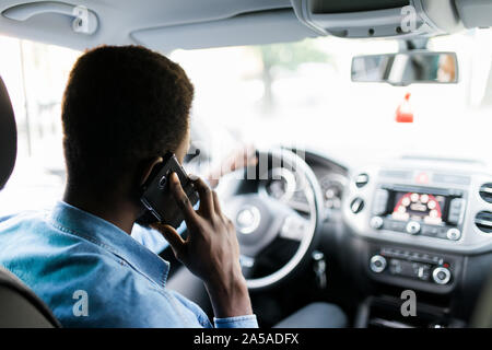 African American man using smartphone making mobile cell call during driving time in luxury car. Stock Photo