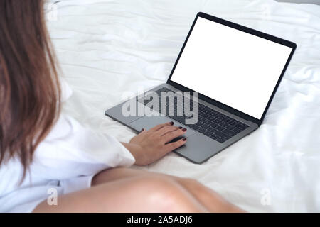 Mockup image of an Asian woman sitting on a bed , using and touching on laptop with blank white desktop screen keyboard Stock Photo